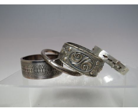 A COLLECTION OF FOUR SILVER AND WHITE METAL BANGLES, to include a sterling silver buckle bangle, a 925 hinged silver bangle w