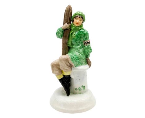 Glossy seated figure of a woman in a green winter coat holding a pair of skis.'Artist original proof for Peggy Davies by Vict