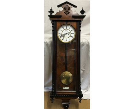 A walnut veneered pendulum wall clock with enamel face and Roman numerals. Case measures approx. 122cms h x 38cms w. Weights 