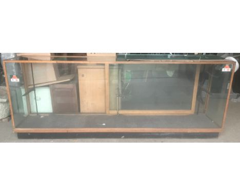 A large oak framed shop counter display cabinet, all sides glass, sliding doors with shelf bracket and glass shelves. 245cm w