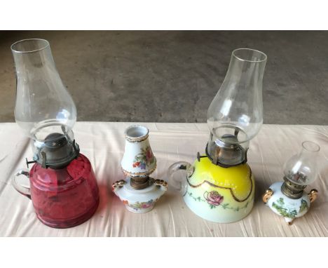 Four oil lamps, one ruby glass, 29cms h including chimney, one yellow white glass floral pattern, and 2 smaller porcelain oil