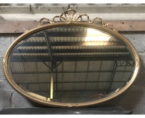 A gilt oval framed bevel edged wall mirror with decorative bow to the top. 88cm w x 65cm h.Condition ReportBreak to bow, silv