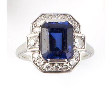 A SYNTHETIC SAPPHIRE AND DIAMOND CLUSTER RING, the rectangular step-cut synthetic sapphire claw set within an octagonal panel