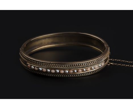 A VICTORIAN CORAL AND HALF PEARL SET BANGLE, of hinged oval design, centred with a line of alternate coral cabochons and half