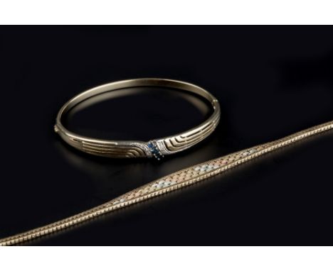 A SAPPHIRE AND DIAMOND SET BANGLE, of hinged oval form with pierced decoration, 9ct gold mounted, and a 9ct three colour gold