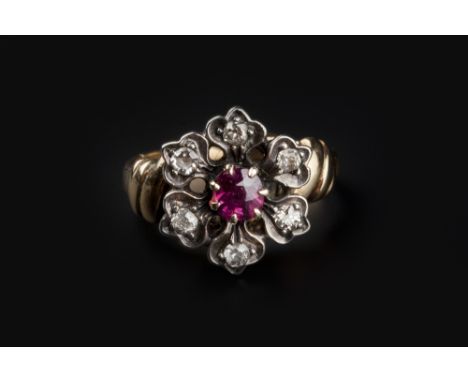 A RUBY AND DIAMOND FLOWERHEAD CLUSTER RING, the cushion-shaped ruby framed by old-cut diamond set petals, between crossover s