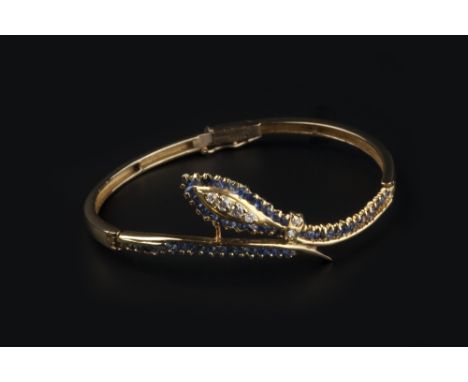A SAPPHIRE AND DIAMOND SET SERPENT BANGLE, of hinged oval form, with brilliant-cut diamond set head and collar, framed by a c