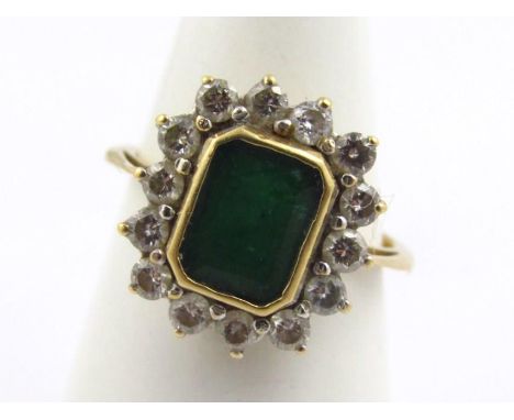 An 18ct gold dress ring, set with rectangular cut emerald, in a rub over settings, surrounded by thirteen round brilliant cut