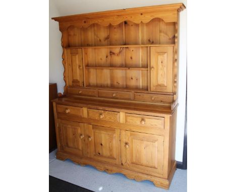 A 20thC stripped and lightly polished pine dresser, the upper section with a carved frieze raised above three Delft racks, se
