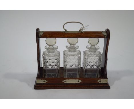 An oak three decanter tantalus, with plated mounts and key