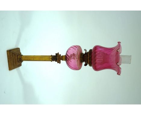 A Victorian brass oil lamp on a Corinthian column with cranberry glass shade and reservoir, 78cm tall