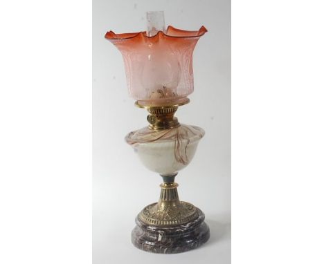 A late Victorian brass pedestal oil lamp, having red tinted acid etched shade, marble glass font, and all raised on marbled p