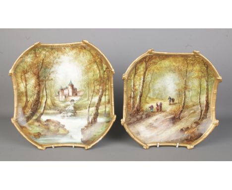 Two hand painted and gilt ceramic wall plaques in the style of Limoges depicting woodland scenes including castle on river. A