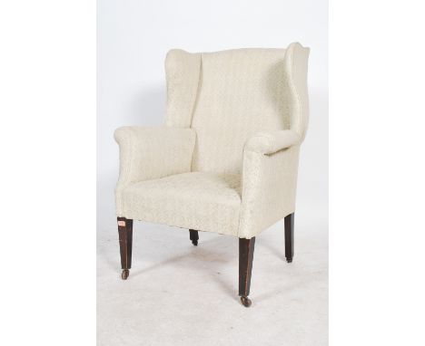 An Edwardian mahogany wingback / Chesterfield style armchair being raised on square tapering legs with brown ceramic castors.