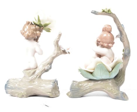 A pair of Lladro ceramic figurines of a male and female cherub mounted on a log with large ceramic flowers. One boxed. Measur