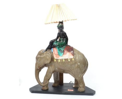 An early 20th century plaster / Chalk ware fairground prize table lamp in the form of an elephant with Moorish lady atop.