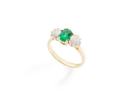 An emerald and diamond three-stone ring claw-set with an oval-cut emerald flanked to either side by a round brilliant-cut dia