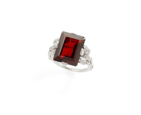 An early 20th century garnet and diamond ring claw-set with a rectangular step-cut garnet, each shoulder modelled as a stylis