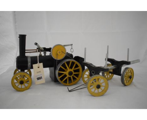 A Mamod live steam traction engine, in black with yellow wheels, the tractor hauling timber carriage.
