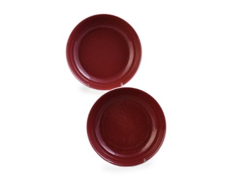 A pair of Chinese copper-red saucer dishes, with shallow rounded sides rising from a slightly tapering foot, both sides cover