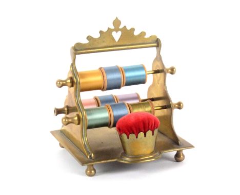 A brass reel stand, the rectangular base on four ball feet and incorporating a pin cushion, the shaped triangular ends with t