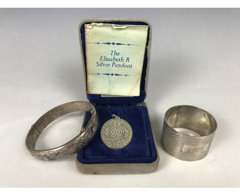 An Elizabeth II commemorative silver pendant, together with a silver hinged bangle and a white-metal napkin ring, stamped 'si