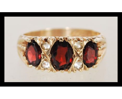 A hallmarked 9ct gold three stone garnet ting having faceted red stones with white stone spacers. Weighs 3.9 grams size N.