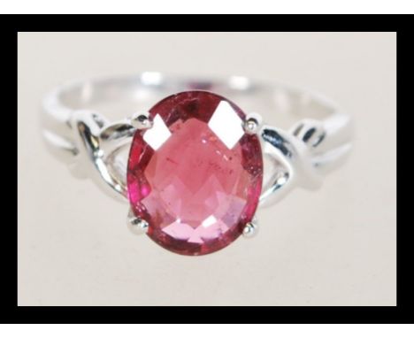A hallmarked 18ct white gold ring prong set with an oval cut Rubellite flanked by two small white accent stones. Hallmarked B