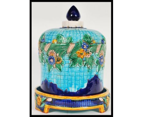 A majolica bell shaped cheese dish and cover. The cover on turquoise ground and decorated with floral swags in relief. The di