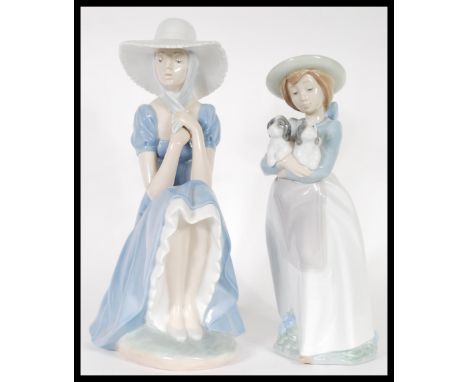 Two Nao porcelain ceramic figures of girls to include a girl seated in a bonnet together with a girl holding two puppies. Bot
