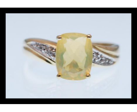 A hallmarked 9ct gold ring prong set with a rectangular yellow stone with white accent stones to the shoulders. Hallmarked Bi