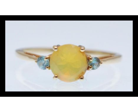 A hallmarked 9ct gold ring prong set with a brilliant cut yellow opalescent stone flanked with two blue accent stones. Hallma