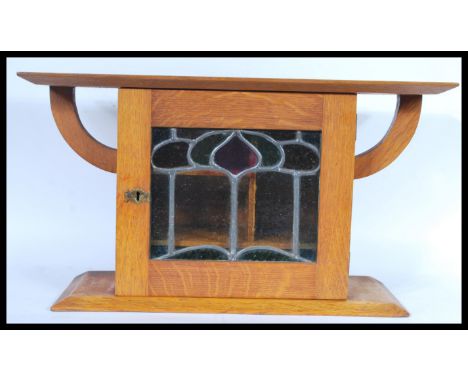 A 19th Century Arts and Crafts light oak Victorian smokers cabinet raised on a plinth base with stained glass panel front. Sh