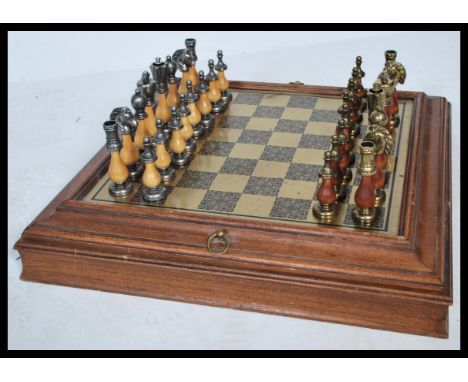 A 20th Century Chess set having a black and gold tone chess board set within a wooden frame with a compartmentalised interior