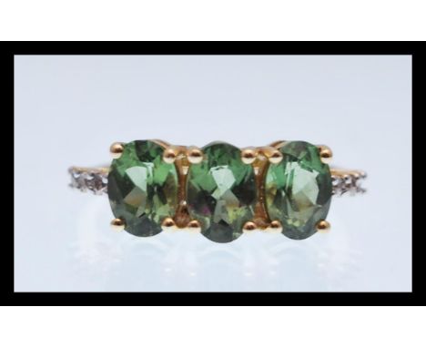 A hallmarked 9ct gold ring prong set with three oval cut green stones with white accent stones to the shoulders. Hallmarked B