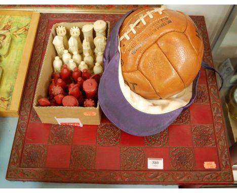 A modern chess board and chess pieces together with a leather football and silk riding hat cover