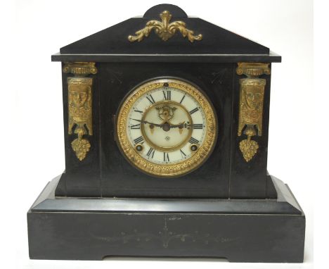 A late Victorian slate mantel clock of architectural form having an enamel dial with Arabic numerals flanked by Egyptian styl