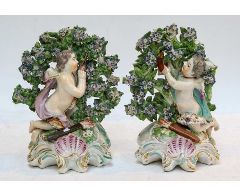 A pair of Chelsea Derby figures, circa 1770, each formed as Cupid kneeling before bocage, one plucking an arrow from the tree