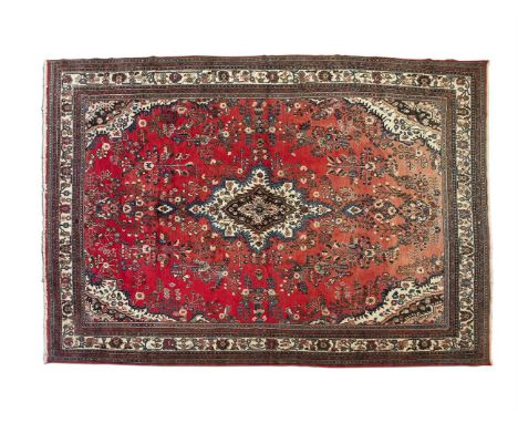 A PERSIAN RED GROUND WOOL CARPET, the all over pattern filled with foliate designs in an open landscape and contained within 