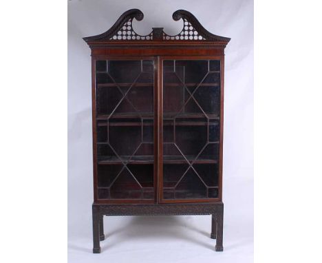 After Chippendale - a mahogany bookcase on stand, having a broken swan-neck architectural pediment over twin astragal glazed 