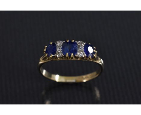 A diamond and sapphire ring, central cushion cut mid blue sapphire flanked by a smaller conforming stone either side, each di