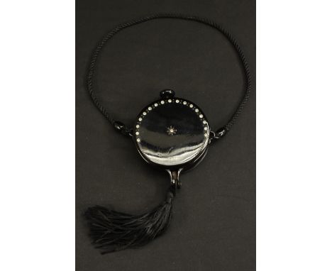 An Art Deco tasseled circular compact, black celluloid, rhinestone set, push button mechanism, internal mirror, cord carrying