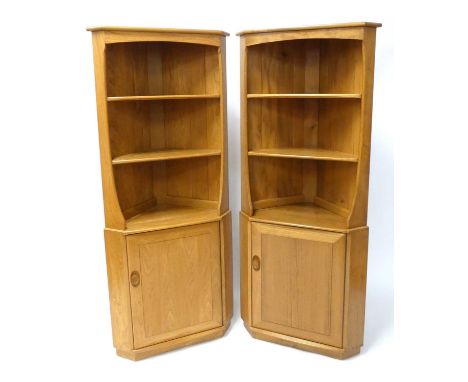 A pair of contemporary Ercol blond elm 'Model 743C' corner cupboards, each having twin open fixed upper shelves over single l