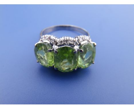 A triple cluster style ring, comprising three pale green stones (centre stone chipped) surrounded by small diamonds on white 