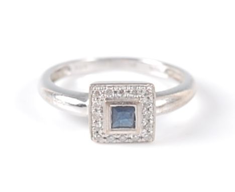 An 18ct white gold, sapphire and diamond square cluster ring, featuring a centre square cut sapphire in a bezel setting, surr