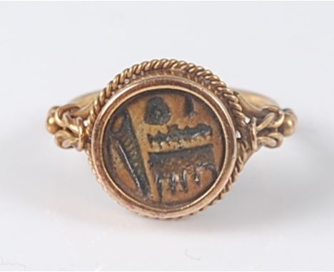 A yellow metal circular signet ring, the ring having a centre intaglio carving of an indistinct pattern within a ropetwist se