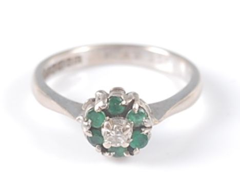 An 18ct white gold, emerald and diamond circular reverse cluster ring, the ring having a centre round brilliant cut diamond w