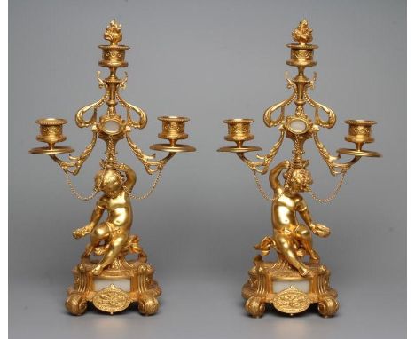 A PAIR OF FRENCH GILT METAL THREE LIGHT FIGURAL CANDELABRA inset with onyx panels, early 20th century, each modelled as a put