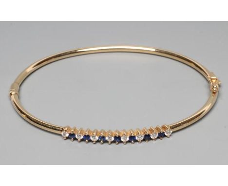 A STIFF HINGED BANGLE, the upper section claw set with seven small sapphires and eight diamonds, to a plain unmarked frame (E