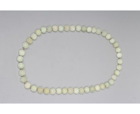 A STRING OF CHINESE CELADON JADE BEADS, the forty six spherical beads carved with scroll and flowers, with gilt metal spacers